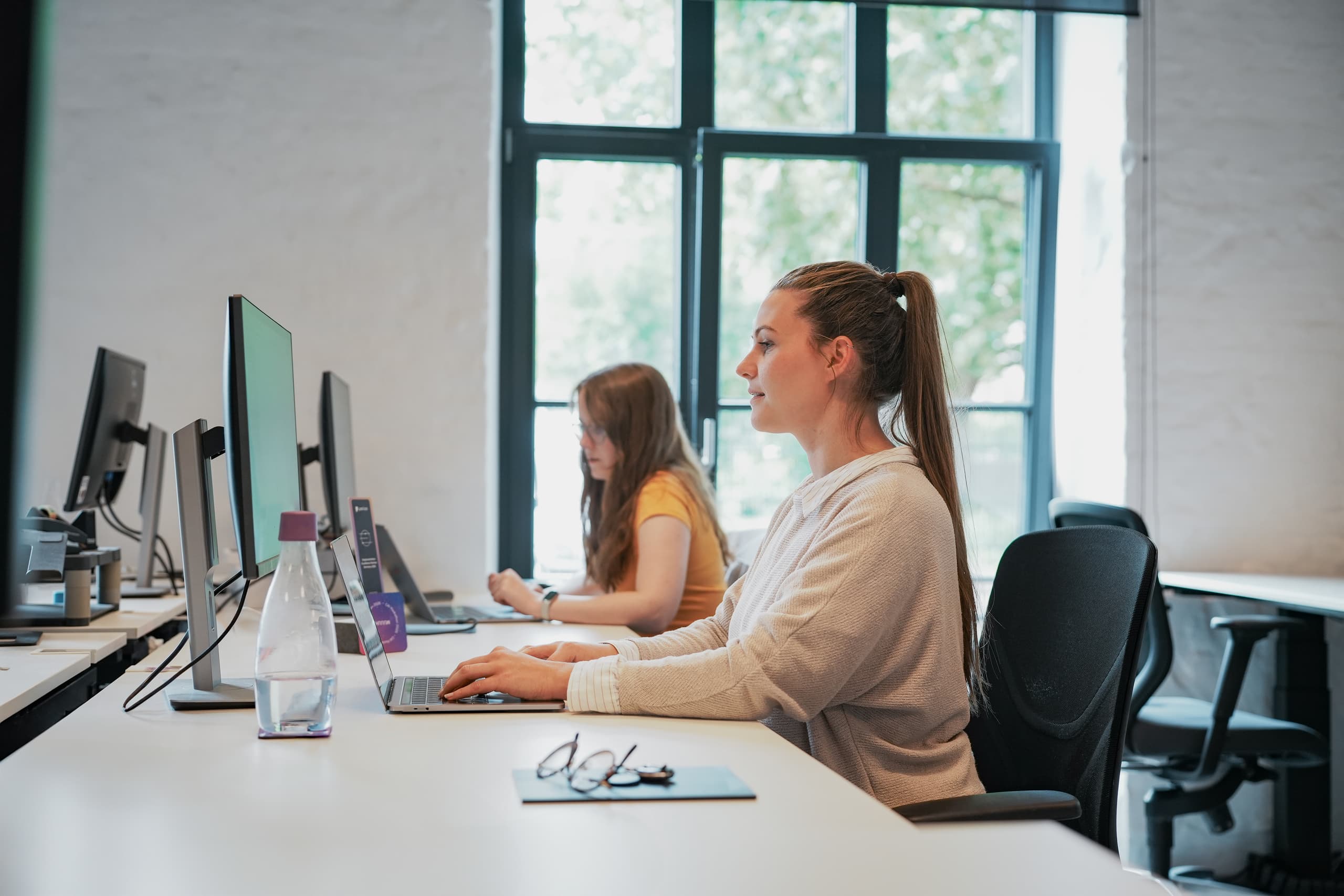 Zwei Mitarbeiterinnen arbeiten konzentriert an Computerarbeitsplaetzen in einem modernen Buero