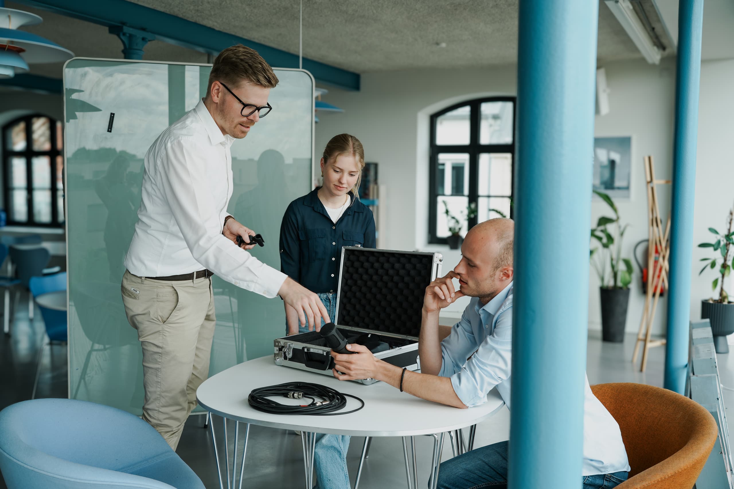 Drei Personen in modernem Büro begutachten gemeinsam ein VR-Headset aus einem Koffer
